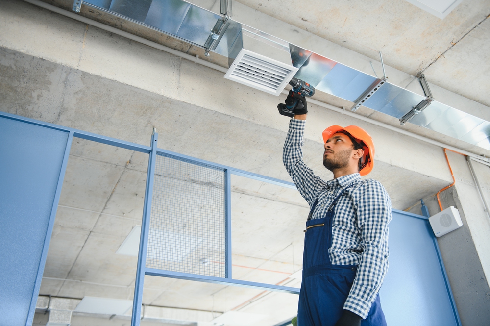 hvac services - indian worker install ducted pipe system for ventilation and air conditioning in house.